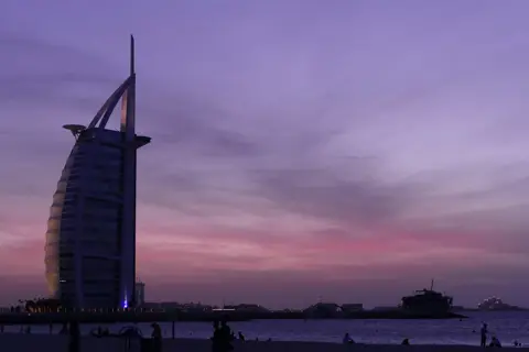 The sail-shaped hotel silhouetted against a purple sunset from the public beach