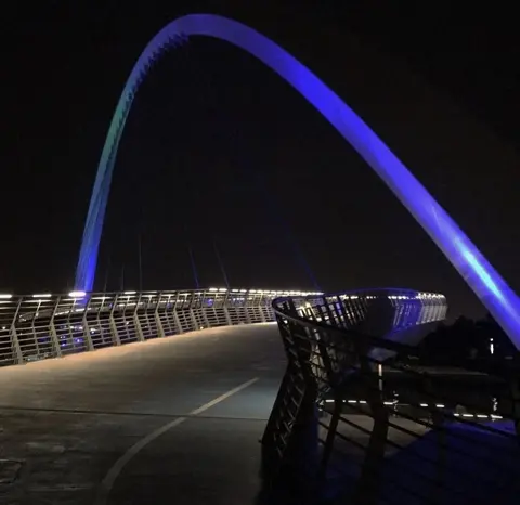 The illuminated arch of a Dubai Water Canal pedestrian bridge at night